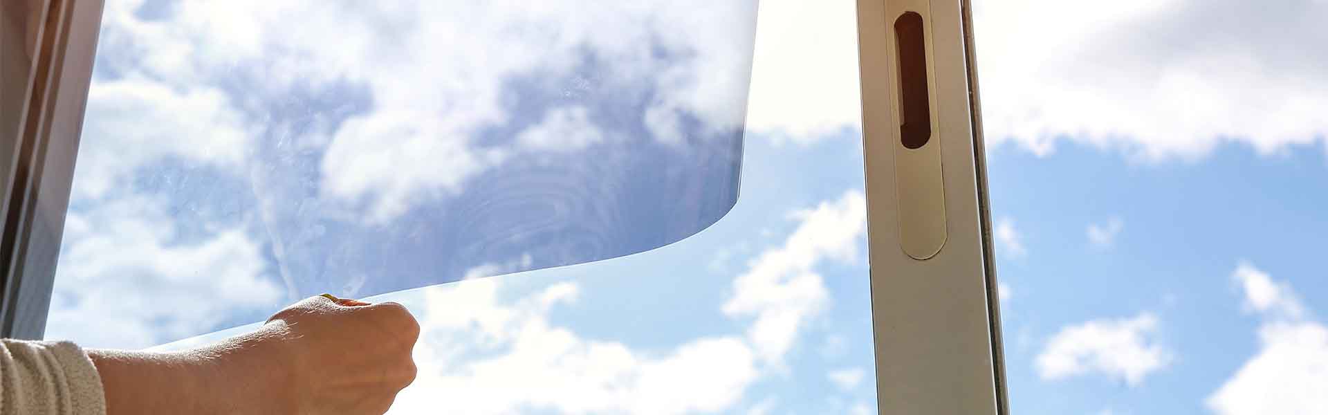 hands holding tint in front of a window from inside the house with a cloud in sky background